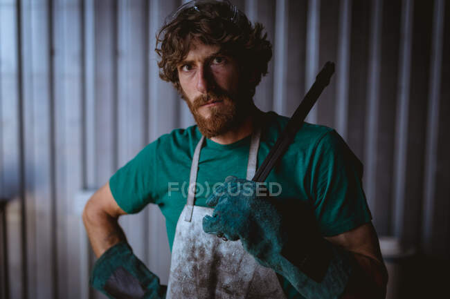 Porträt eines selbstbewussten bärtigen Schmieds, der Werkzeug in der Hand hält, während er in der verarbeitenden Industrie steht. Schmiede-, Metall- und Fertigungsindustrie. — Stockfoto