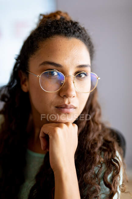 Ritratto ravvicinato di donna d'affari biraciale sicura con mano su mento in occhiali a ufficio. affari creativi e ufficio moderno. — Foto stock