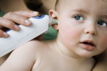 Крупним планом мати приймає температуру дитини з вушним термометром — стокове фото
