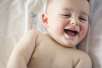Portrait of cute shirtless baby boy laughing while lying on bed — Stock Photo