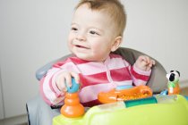 Cheerful baby boy sitting in baby-walker and looking away — Stock Photo