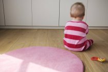 Rear view of baby boy in striped pajamas sitting on floor and playing — Stock Photo