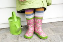 Close-up of little girl in rubber boots standing next to green watering can — Stock Photo