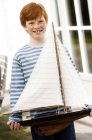 Рыжий мальчик держит модель лодки и смотрит в камеру — стоковое фото