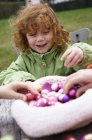 Маленькая рыжая девочка играет с пасхальными яйцами на открытом воздухе — стоковое фото