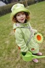 Kleines Mädchen im Regenmantel steht im Garten und hält Gießkanne in der Hand — Stockfoto