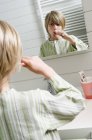 Portrait de garçon souriant brossant les dents devant le miroir dans la salle de bain — Photo de stock