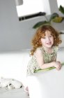 Портрет улыбающейся рыжей маленькой девочки, опирающейся на мыло дома — стоковое фото
