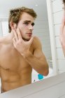 Uomo senza maglietta guardando specchio bagno — Foto stock