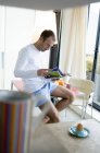 Mann sitzt auf Küchentisch, liest Magazin, Tasse und gekochtes Ei im Vordergrund — Stockfoto