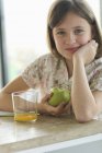 Portrait of smiling little girl eating apple at table — Stock Photo
