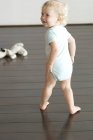 Smiling little boy walking on wooden floor and looking away — Stock Photo