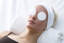 Portrait of young woman with beauty mask on face and cleansing cotton pads on eyes — Stock Photo