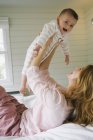 Giovane donna sdraiata sul letto, tenendo il bambino e ridendo — Foto stock
