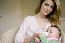 Portrait de mère nourrissant bébé au biberon à la maison — Photo de stock