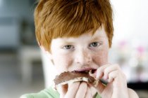 Portrait of redheaded little boy eating a slice of bread and chocolate — Stock Photo