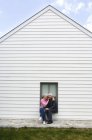Senior couple embracing, sitting on window sill of white house — Stock Photo