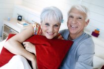 Lächelndes Seniorenpaar, das zusammen auf dem Bett sitzt und in die Kamera schaut — Stockfoto