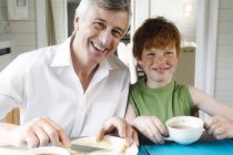 Smiling senior man and boy having breakfast in kitchen — Stock Photo