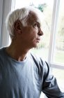 Thinking senior man looking through window — Stock Photo