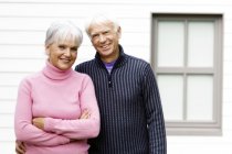 Retrato de pareja mayor sonriente de pie frente a la casa - foto de stock
