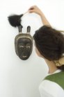 Frau staubt ethnische Maske mit Staubwedel ab — Stockfoto