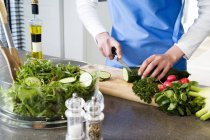 Primo piano di mani femminili che fanno l'insalata, il cetriolo di taglio su cima di tavolo di cucina — Foto stock