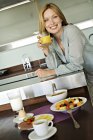Mulher sorridente segurando suco de frutas na mesa na cozinha — Fotografia de Stock