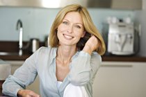 Smiling woman with hand in hair looking at camera in kitchen — Stock Photo