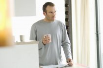 Thoughtful man standing in kitchen and holding mug — Stock Photo