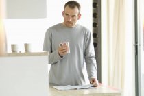 Thoughtful man standing in kitchen and holding mug — Stock Photo