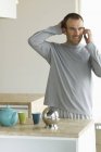 Mann steht in Küche und telefoniert mit Handy — Stockfoto