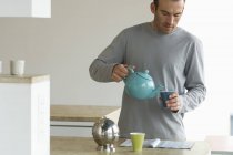 Mann steht in Küche und gießt Tee in Tasse — Stockfoto