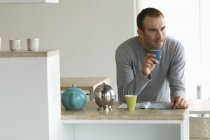 Thoughtful man standing in kitchen and holding glass — Stock Photo