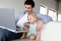 Hombre y niño pequeño usando ordenador portátil - foto de stock