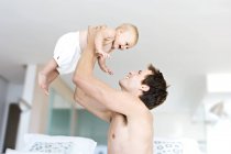 Отец держит весёлого ребенка играющего в спальне — стоковое фото