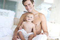 Retrato de padre feliz y niño sentado en la cama - foto de stock