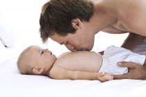 Portrait of father kissing baby chest on bed — Stock Photo