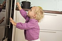 Маленькая девочка открывает холодильник на кухне — стоковое фото