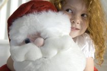 Portrait de gingembre petite fille tenant un jouet câlin Père Noël — Photo de stock