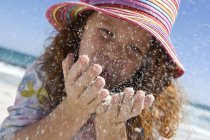Portrait of little girl blowing sand in hands on beach — Stock Photo