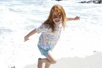 Cheerful ginger little girl having fun on beach — Stock Photo