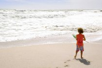 Niño pequeño parado en la playa y sosteniendo la red de aterrizaje - foto de stock