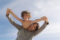 Retrato de un padre llevando a su hijo en la espalda, al aire libre - foto de stock