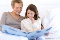 Seniorin und kleines Mädchen im Bett, Blick auf Fotoalbum — Stockfoto