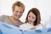 Senior woman and little girl in bed, looking at photograph album — Stock Photo