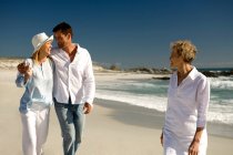 Couple embracing and senior woman waking on the beach — Stock Photo