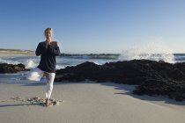 Lächelnde junge Frau in Yoga-Attitüde am Strand — Stockfoto