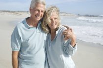 Smiling mature couple embracing on sandy beach — Stock Photo