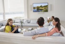 Casal assistindo televisão com filhas ocupadas com gadgets — Fotografia de Stock